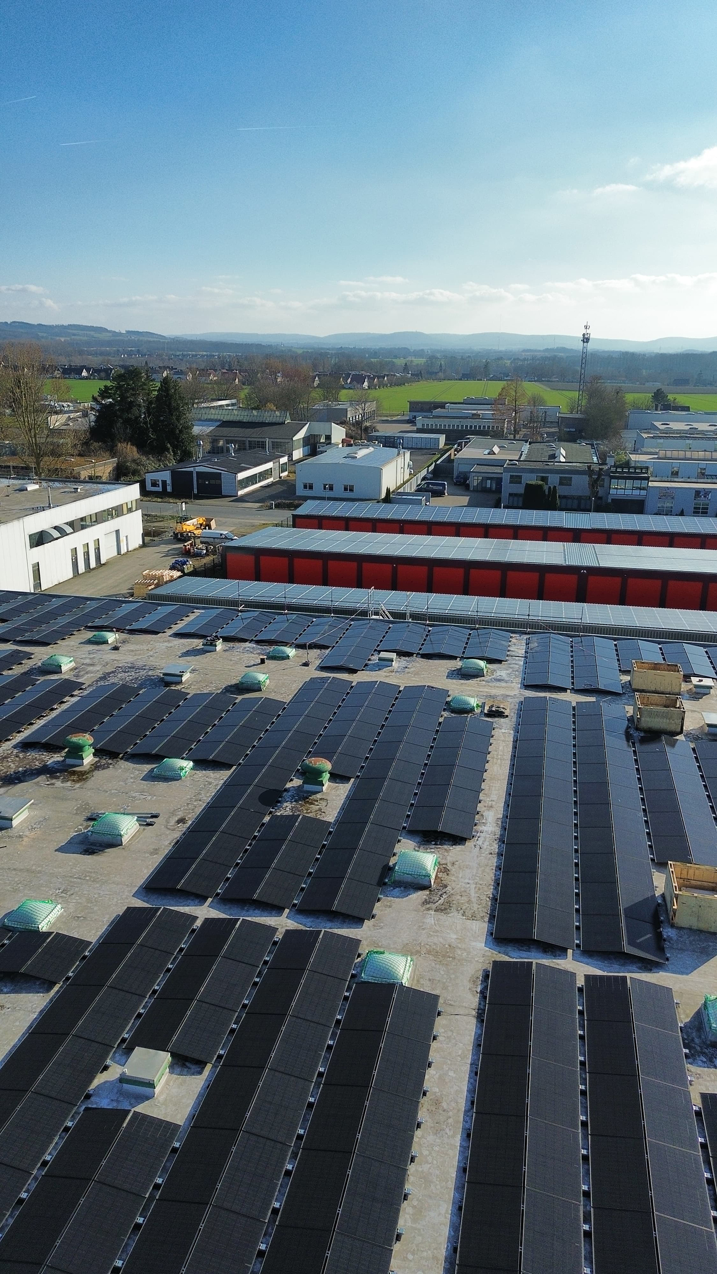 Solaranlage-Gewerbe_SolarenergiePLUS Eine großflächige Solaranlage auf den Dächern eines Gewerbeareals. Die Module sind in langen Reihen montiert und umgeben von Hallen und Betriebsgebäuden.
