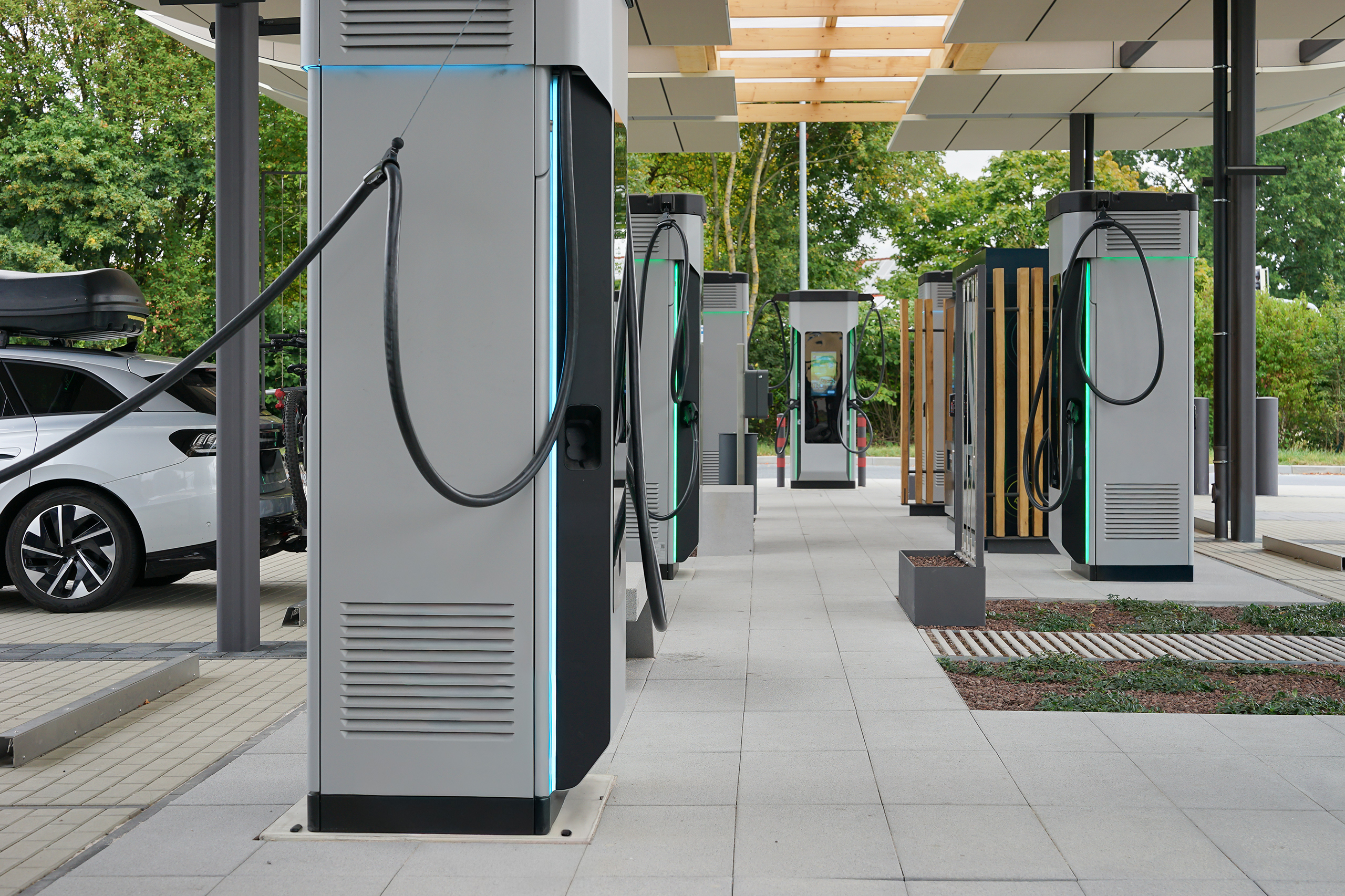 Gewerbekunden_Ladeparks Eine Reihe moderner Ladesäulen für Elektrofahrzeuge an einem überdachten Ladepark. Ein geparktes Auto steht seitlich neben den Säulen.
