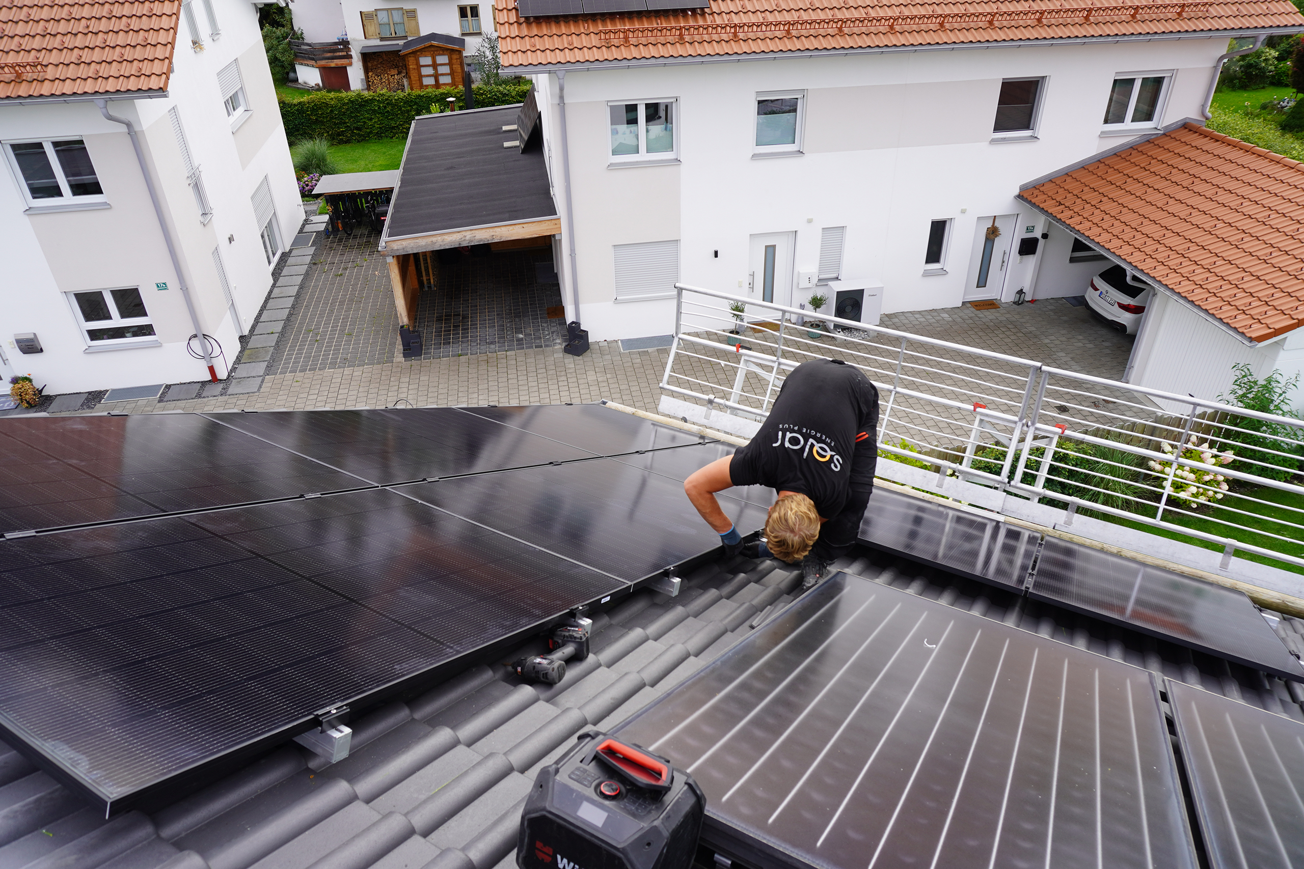 Privatkunden_Photovoltaik_Montagesystem Ein Monteur installiert ein Photovoltaik-Montagesystem für Privatkunden auf dem Dach eines Wohnhauses. Die umliegenden Gebäude der Wohnsiedlung sind im Hintergrund sichtbar.