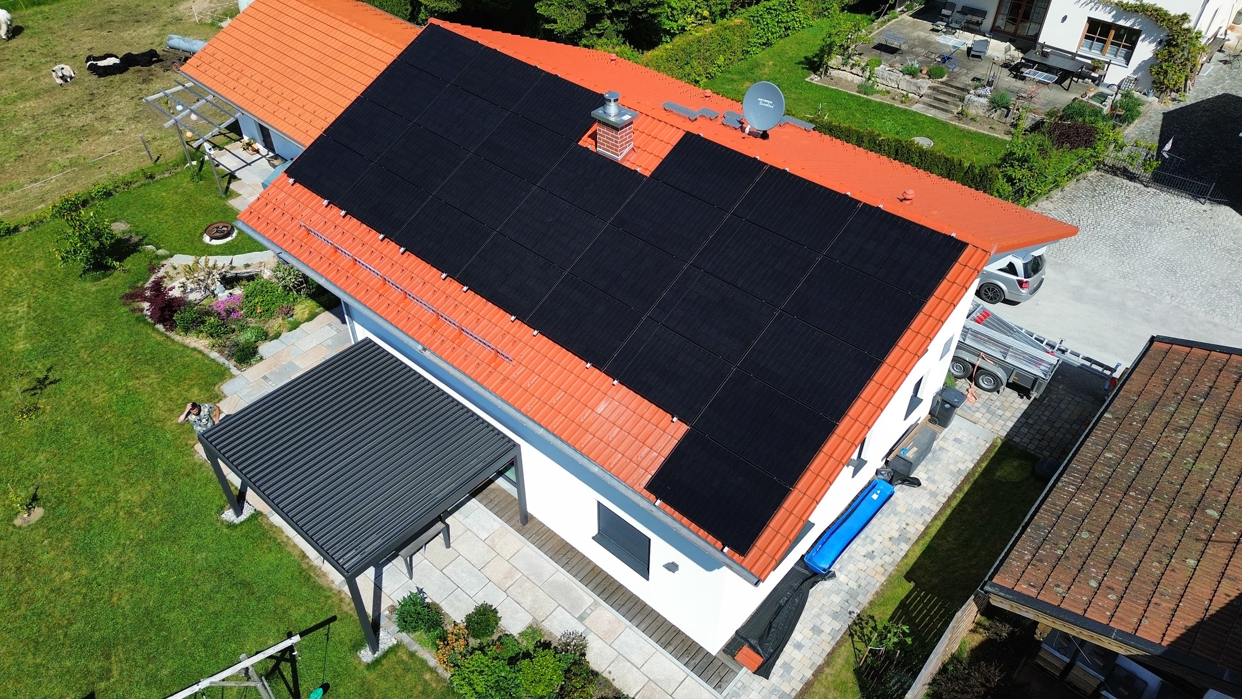 Solaranlage_Photovoltaik Eine großflächige Photovoltaikanlage auf dem Dach eines Wohnhauses. Der grüne Garten umgibt das Gebäude.